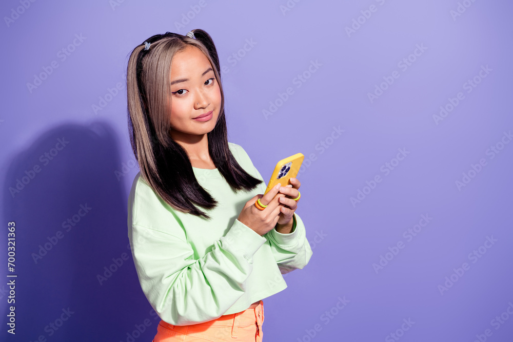 Photo of japanese youngster student girl with brunette hair ponytails using mobile phone for blogging isolated on violet color background Photo of japanese youngster student girl with brunette hair ponytails using mobile phone for blogging isolated on violet color background