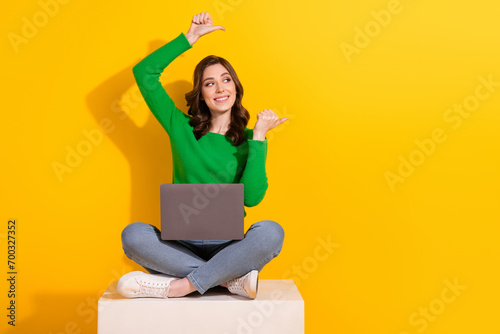 Full body photo of woman brunette curly hair programmer sit cube with netbook point fingers novelty isolated on yellow color background