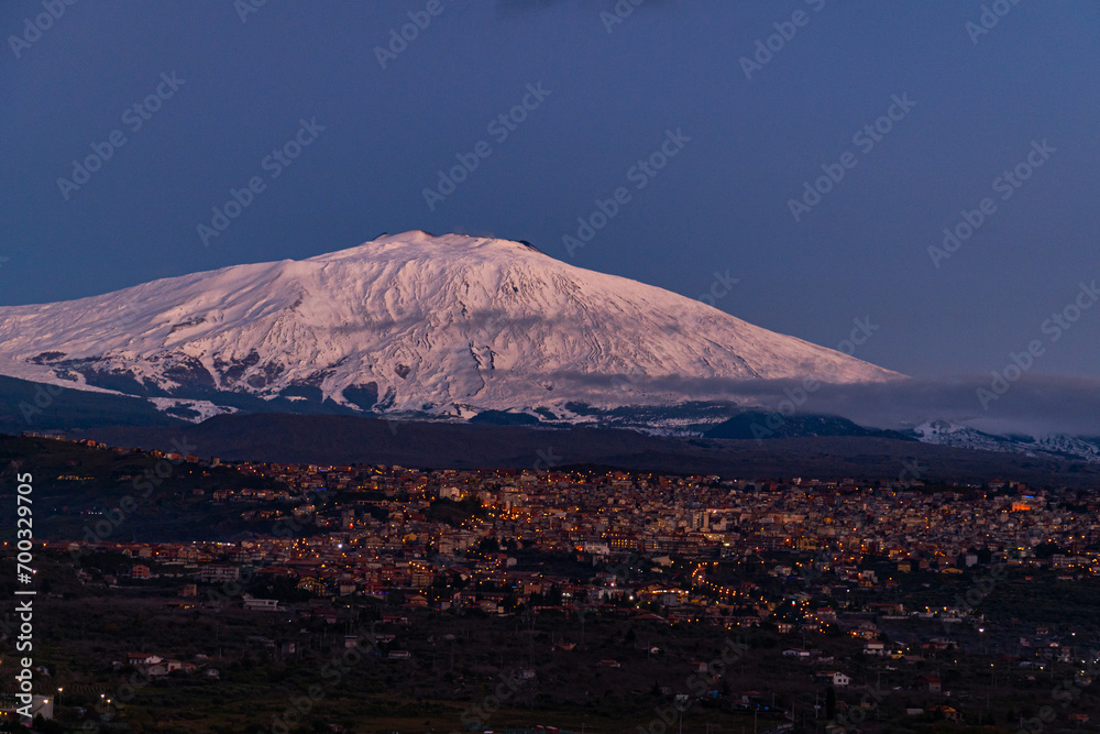 Bronte town under the snowy and majestic volcano Etna and a cloudy blue sky