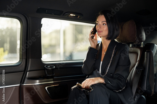 Business lady in formal black wear talks on phone while sitting in luxury taxi. Concept of business during transportation