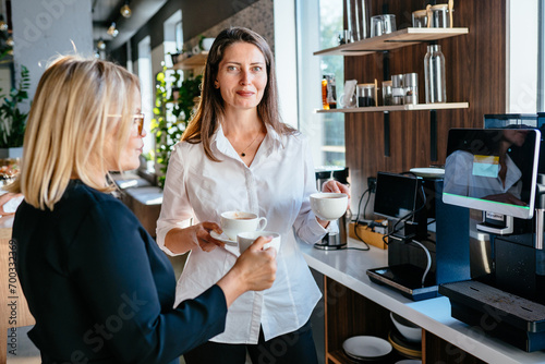 Two mature businesswomen discussing during coffee break. Mature businesswoman on coffee break in office kitchen, holding coffee. photo