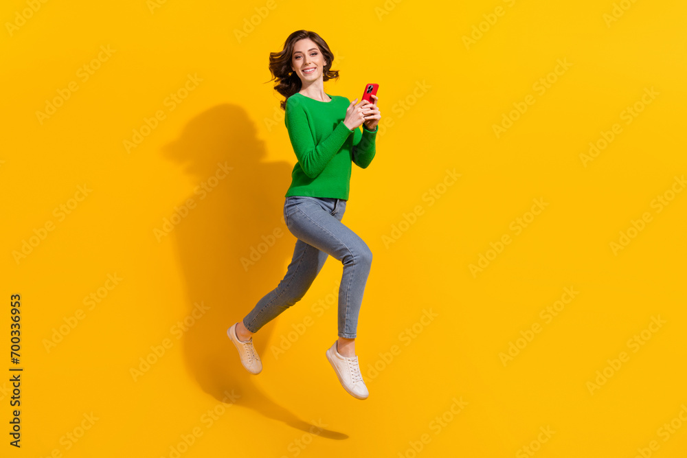 Full body length photo of cheerful young energetic lady green pullover jeans addicted using cellphone isolated on yellow color background