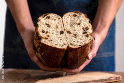 hands holding big homemade sourdough bread with seeds and cereals and bread knife cutting into slices photo