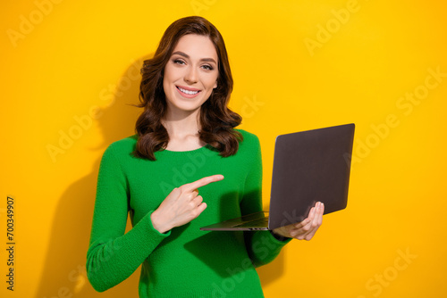 Portrait of pretty positive girl beaming smile indicate finger arm hold netbook isolated on yellow color background