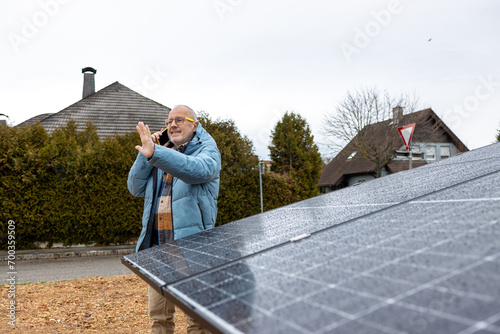 Smiling  senior businessman examining solar panel while talking by telephone 