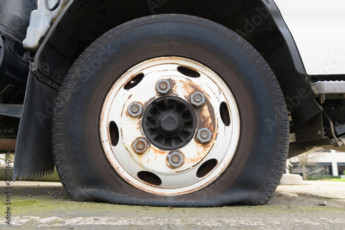 Flat truck tire on axel with rust on wheel hub with deflated tire on ground photo