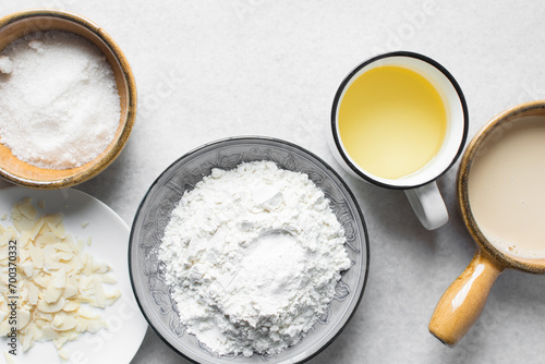 mise en place of ingredients for making vanilla almond muffins, top view of sugar, eggs, oil, flour milk on a marble table, process of making vanilla almond muffins