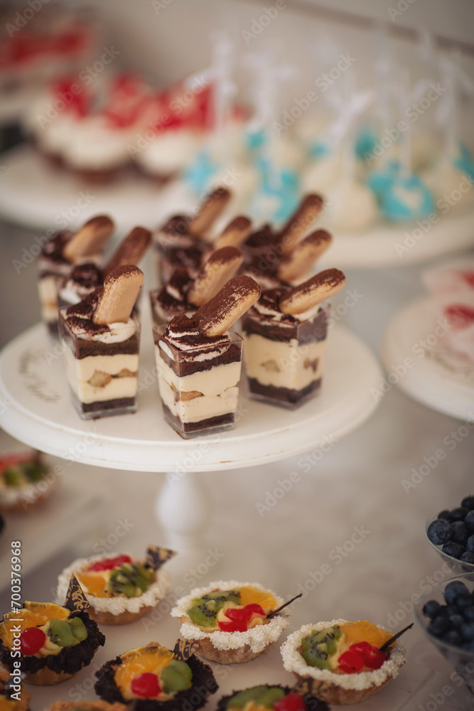 Fototapeta premium Closeup of many small cakes, sweets, fruits served on plate for cocktail party. Candy bar on birthday or wedding holiday dinner. catering food. tasty dessert. Wedding banquet table. Fruit bar on party