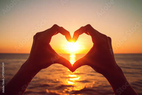 Hands Forming a Heart Shape Against Ocean Sunset