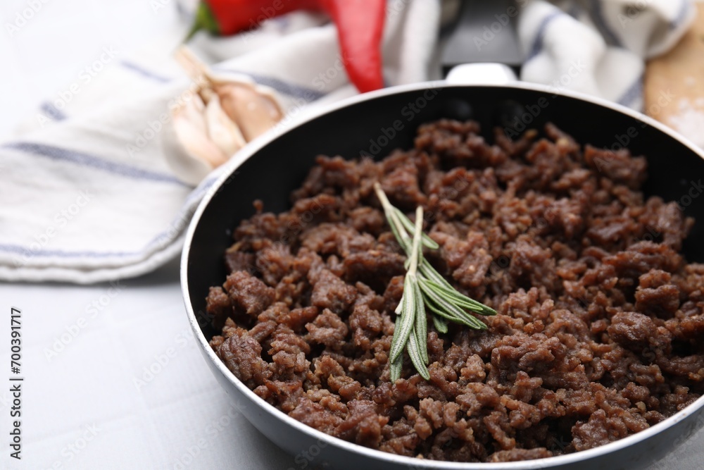Fried ground meat in frying pan and rosemary on white tiled table, closeup Fried ground meat in frying pan and rosemary on white tiled table, closeup