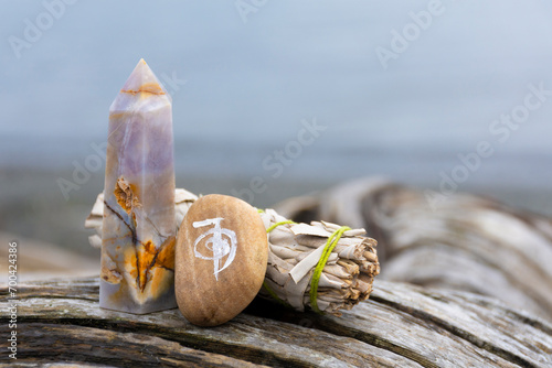 An image of a healing reiki symbol with white sage smudge stick and crystal tower on an old weathered driftwood log.  photo