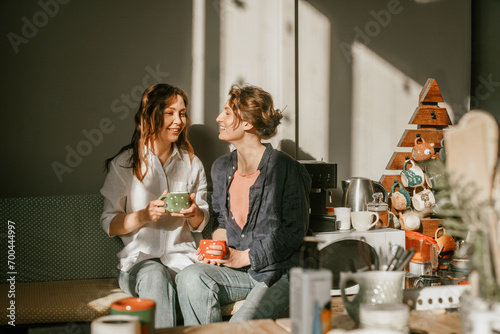 Two female friends enjoying morning coffee in a cozy home kitchen Sunny morning and friendly conversations between two young women photo