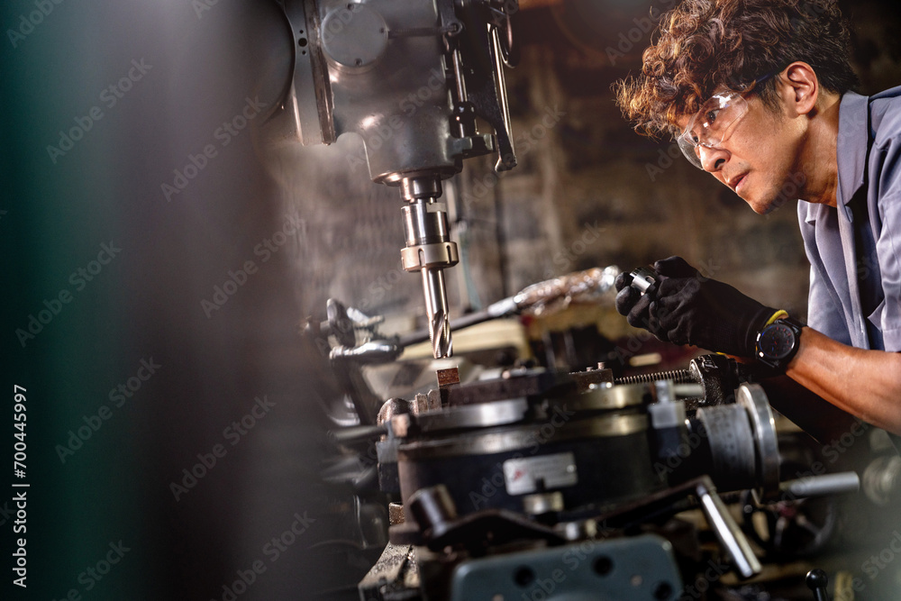 Obraz premium Asian worker in production plant drilling at machine. Professional worker near drilling machine on factory. finishing metal working internal steel surface on lathe grinder machine with flying sparks.