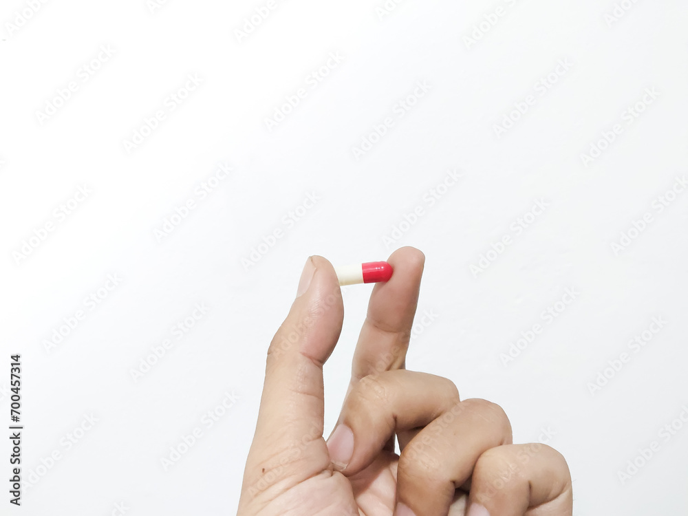 Fingers of a hand holding a capsule pill isolated on a white background Fingers of a hand holding a capsule pill isolated on a white background