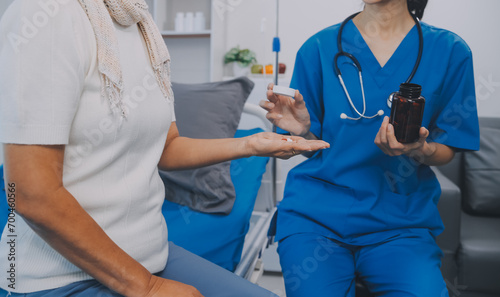 Asian woman nurse holding a medicine bottle and telling information to Asian senior woman before administering medication. Caregiver visit at home. Home health care and nursing home concept.