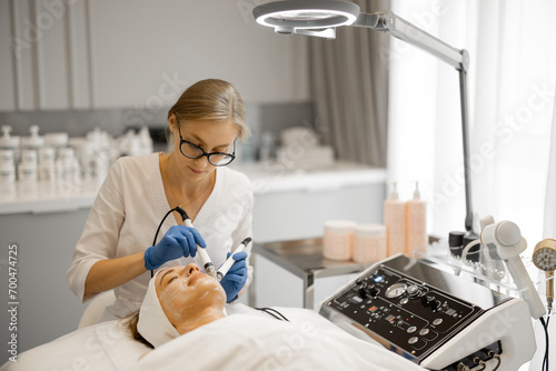 Quadro su tela Young beautician doing microcurrent therapy on a client's face in beauty salon