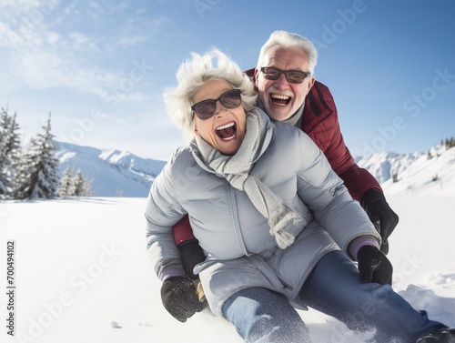Happy senior couple having fun spending winter vacation in mountains sledding down the slope on a snowy mountain