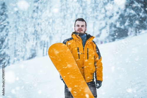 Snowboarding on a winter day. A young man with a beard with his snowboard on a white slope. He is having fun and feeling the adrenaline. The background is a stunning view of the snowcovered pines.
