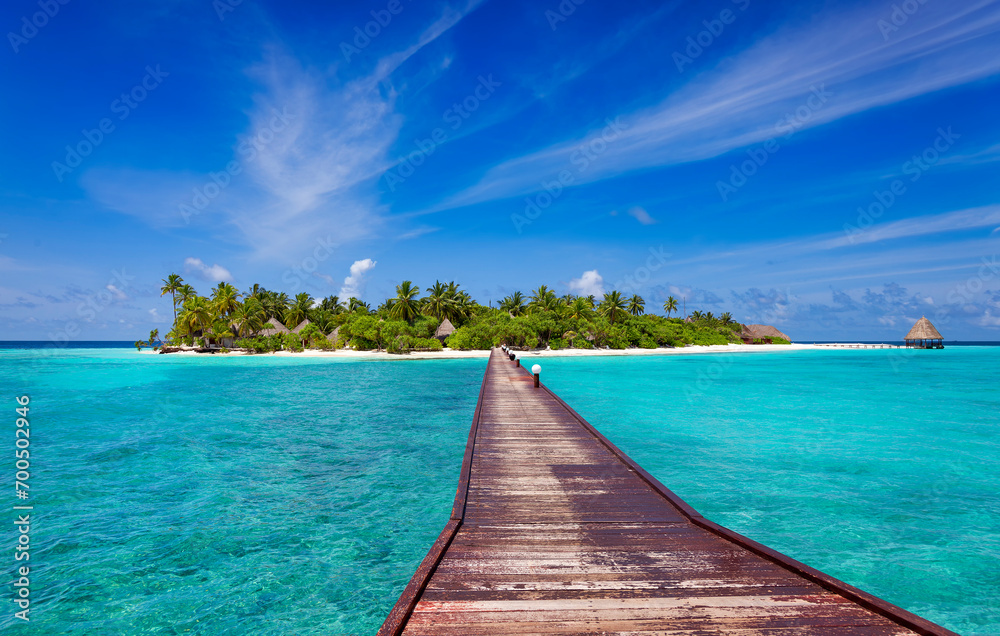 Jetty over blue ocean leading to sandy beach of tropical island, beautiful sky, green palm trees, maldives islands