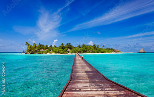 Jetty over blue ocean leading to sandy beach of tropical island, beautiful sky, green palm trees, maldives islands photo