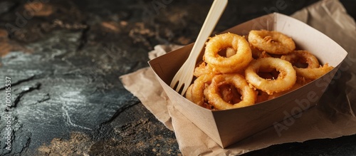 Battered onion rings takeaway in a cardboard tray with a wooden fork Biodegradable plastic free eco friendly takeaway container. Creative Banner. Copyspace image