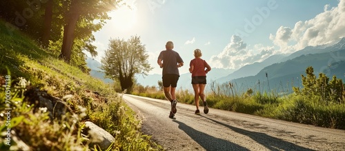 Full length rear view of two healthy senior people jogging on a country road against clear blue sky in summer. Creative Banner. Copyspace image
