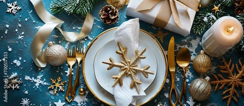 Christmas festive table setting with white plates and gold cutlery white linen napkin gifts in white and gold paper wooden snowflake decoration paper decorations and balls Flatlay blue and gold