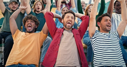 Cheerful mixed race people doing wave together at stadium during soccer match. Happy fans smiling and shouting loudly something. Football game. Entertainment. Sport event concept.