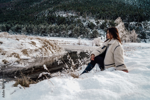 Stylish beautiful woman sitting in the snow, with a stunning snowy landscape in the background