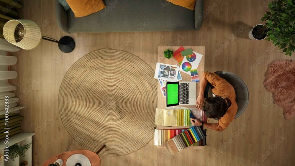 Obraz premium Top view capturing a man working in his home office. Young designer is looking through, comparing the textile color samples for his project and inserting data into his laptop.