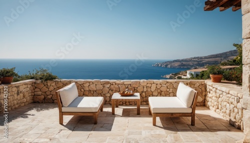  a couple of chairs sitting on top of a stone patio next to a stone wall and a body of water on the other side of the cliff side of the ocean.