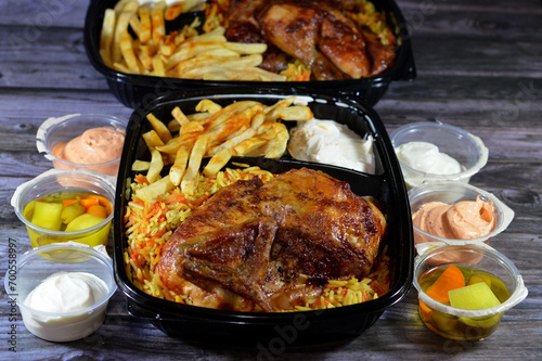 Arabic Syrian cuisine of machine grilled barbecued chicken with colorful Basmati rice and French fries finger potatoes served in a black disposable plate served with garlic sauce, selective focus photo
