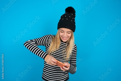 beautiful caucasian teen girl wearing striped sweater holding in hands cell playing video games or chatting