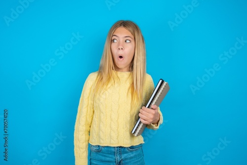 Shocked beautiful caucasian teen girl wearing yellow sweater look empty space with open mouth screaming: Oh My God! I can't believe this.
