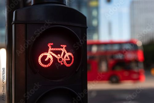 A red cycle lane traffic stop signal at a junction in a busy London city street with a double decker bus passing in the background.