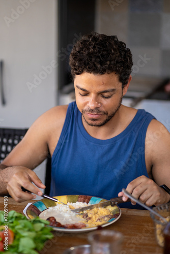 Positive latino man having traditional brazilian lunch at home, sitting at kitchen table, copy space 