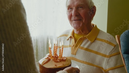 Old man looking at birthday cake and blowing candles