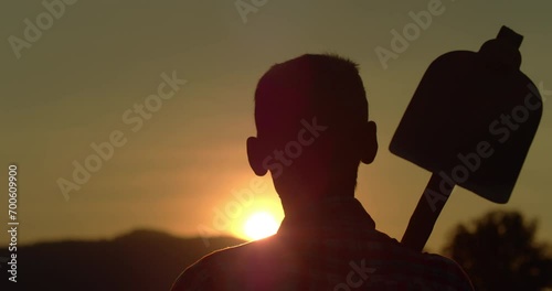 Slow motion scene at sunset with flare of sunlight as Asian farmer who is a poor man in the countryside carrying a hoe who had just finished working in the farm and was about to return home.