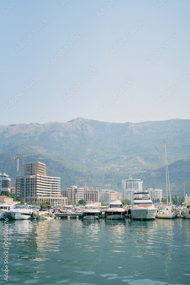 Row of yachts moored off the coast with high-rise buildings at the foot of the mountains