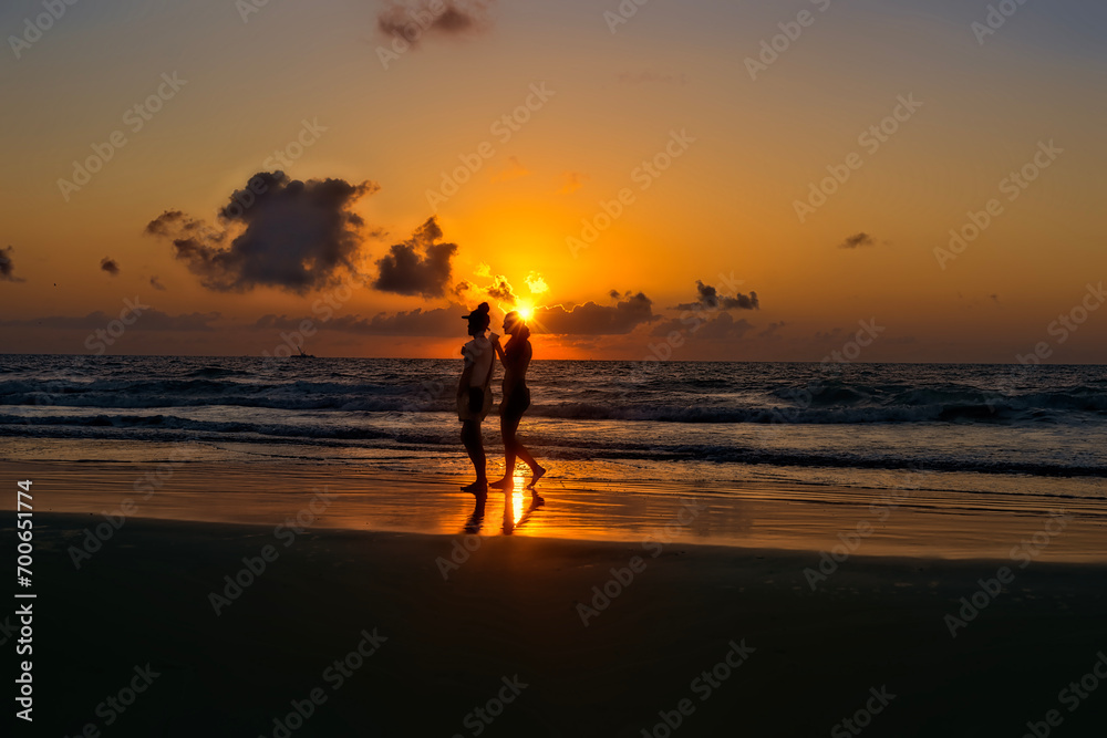 Two women walking along shore at sunrise