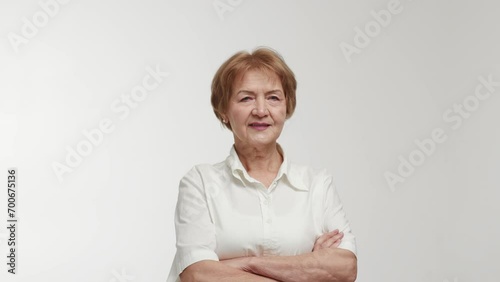 An elderly businesswoman or entrepreneur with a direct gaze and ironic smile on face crosses arms over chest, demonstrates confidence and authority. Showcasing of defensive psychological pose and photo