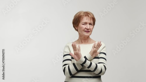 An elderly woman pulls a face with contempt and disgust, shows emotions of discontent, disapproval and inadmissibility. Gesture with crossed palms, sign of prohibition, categorical rejection photo