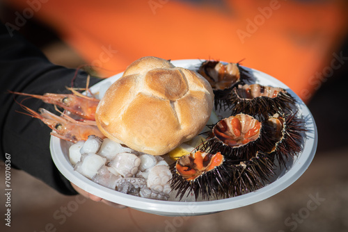 Plate with open sea urchins, raw pieces of octopus, cuttlefish and shrimp or scampi ready to eat with bread in a street food market in Bari, Puglia, Italy