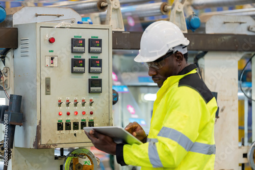 Electronic circuit boards for machinery in plastic and steel industries There is an African male engineer standing and inspecting the company's business systems, wearing a safety vest and helmet.