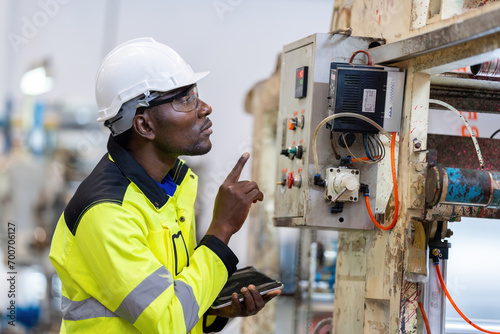 African male engineer department head Point to the electronic circuit board. of machinery in plastic and steel industries Wear a safety helmet and vest. holding laptop to work