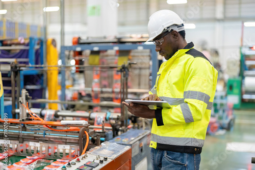 African male engineer standing in engine room Using a laptop to control a material production machine system, working in a plastic and steel industry regarding the company's product business. photo