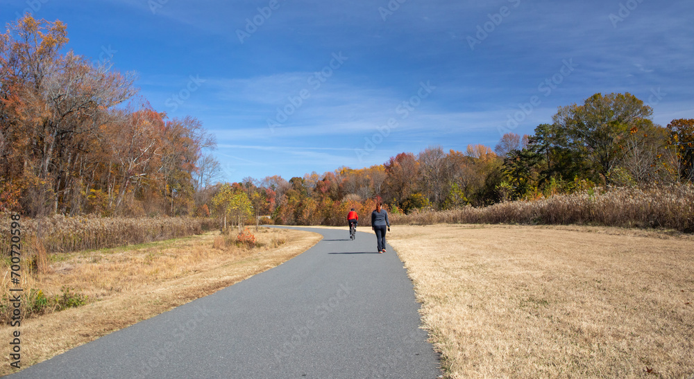 A bicyclist and walker on a paved trail in autumn A bicyclist and walker on a paved trail in autumn