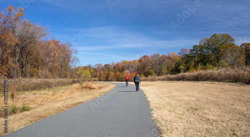 A bicyclist and walker on a paved trail in autumn