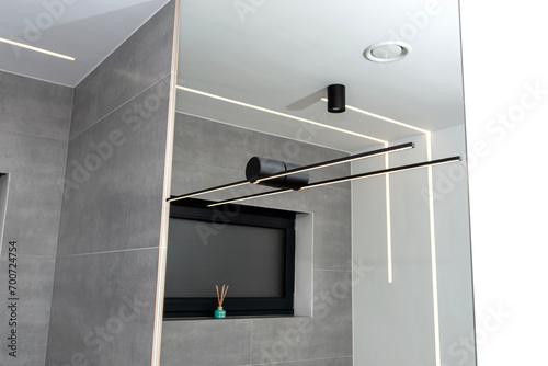 LED light strips mounted in the wall and ceiling in a modern bathroom, visible black wall lamp. photo