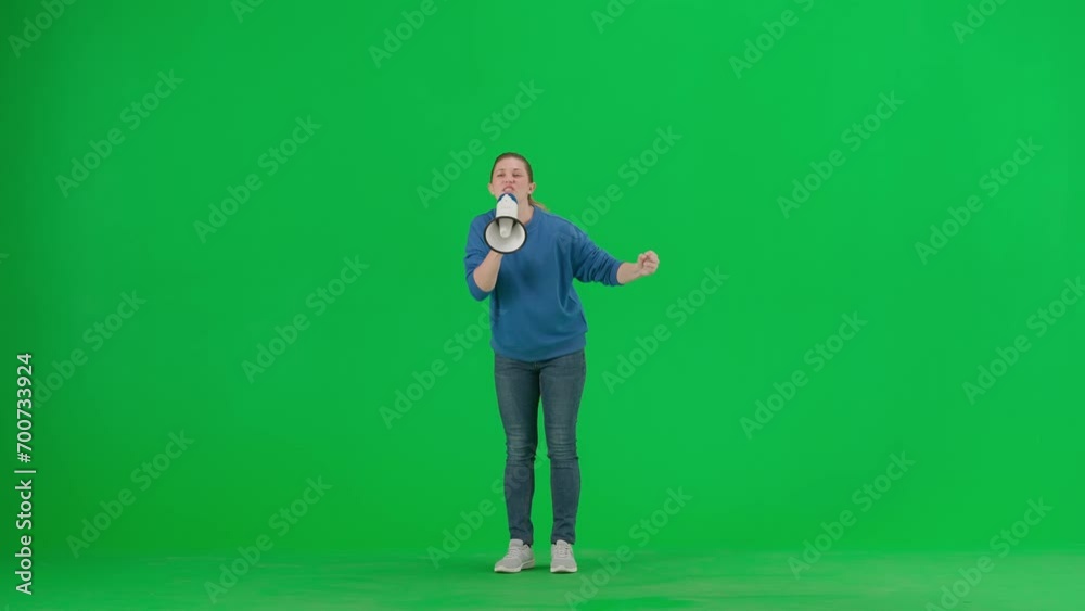 Female activist with raised fist shouting menacingly into megaphone in studio on green screen. Front view of a pro protest woman. Protest action, fight for women's rights, strike. Female activist with raised fist shouting menacingly into megaphone in studio on green screen. Front view of a pro protest woman. Protest action, fight for women's rights, strike.